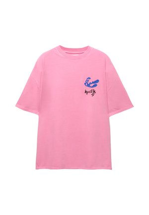 Roze katoenen t-shirt met een ontspannen pasvorm. Heeft een blauwe golfafbeelding en zwarte tekst op de linker borst. Korte mouwen en ronde hals.