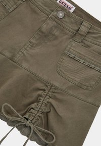 Olijfgroene shorts met elastische ruches in de taille, kanten afwerking langs de zoom en twee voorkanten zakken. Zichtbare details van metalen knopen en stiksels.