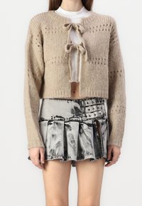 Beige pletený svetr s ribovanou texturou a zavazováním, zkombinovaný s plisovanou sukní s černobílým flekováním, která má více přezek.