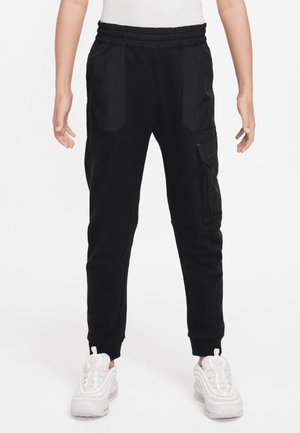 Person iført sorte cargo joggerbukser med elastisk talje og lommer, kombineret med hvide sneakers og en hvid top.