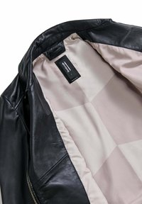 Giubbotto in pelle nera con una texture liscia, chiusura con zip e una fodera interna a scacchi di colore chiaro con etichetta per la cura del tessuto.