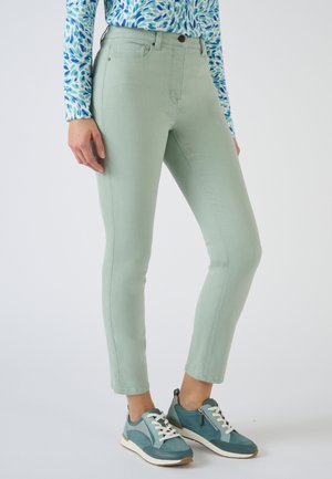 Lichtgroene skinny jeans met een gladde textuur en klassiek vijf-pocket ontwerp, gecombineerd met teal sport schoenen met witte veters.