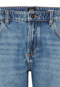 Luźne niebieskie dżinsy z zapięciem na guzik, widocznym szwem i dwoma frontowymi kieszeniami. Średnie pranie z lekko teksturowaną powierzchnią.