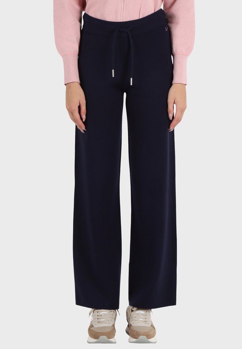 Pantaloni larghi blu scuro in un materiale morbido con elastico in vita, abbinati a una maglietta rosa chiaro e scarpe da ginnastica beige.
