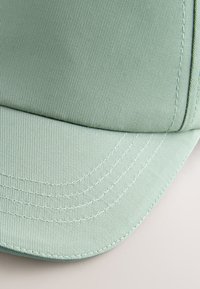 Casquette de baseball vert clair avec coutures détaillées sur la visière incurvée, présentée sur un fond clair.