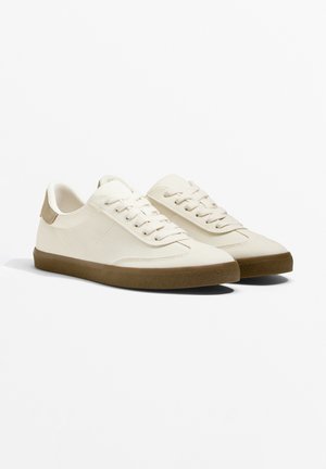 Helle beige Canvas-Sneaker mit einer strukturierten braunen Gummisohle. Zu den Merkmalen gehören eine runde Zehenpartie, ein Schnürdesign und ein Akzent aus Wildleder an der Ferse.