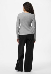 Haut gris à manches longues avec un corsage ajusté et un ourlet en peplum, associé à un pantalon large noir, vu de dos.