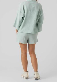 Světle mátově zelený texturovaný outfit s volným topem s krátkým rukávem a odpovídajícími kraťasy, doplněný krémovými vysokými teniskami.