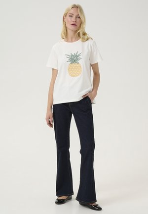 White cotton T-shirt with a yellow pineapple graphic at the center, paired with dark flared jeans and black flats. Simple design, casual fit.