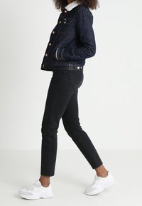 Dark denim jacket with a white fleece collar, paired with black jeans and white sneakers. Features copper buttons and pockets.