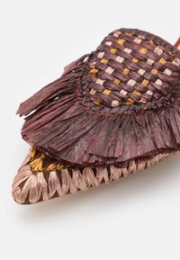 Sandale tissée pointue avec détail de franges superposées dans des tons marron, beige et or sur fond blanc.