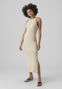 Knit beige dress with diamond pattern, sleeveless design, slim fit, side slit, styled with flat brown sandals.