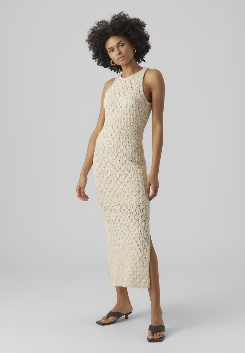 Knit beige dress with diamond pattern, sleeveless design, slim fit, side slit, styled with flat brown sandals.