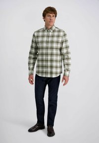 Groene en witte geruite overhem met lange mouwen, knoopsluiting bij de kraag, en een relaxte pasvorm, gecombineerd met donkerblauwe jeans en bruine schoenen.