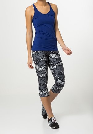 Blå tætsiddende tanktop med tynde stropper, parret med capri leggings i sort og grå camouflage mønster. Modellen bærer sorte atletiske sko.
