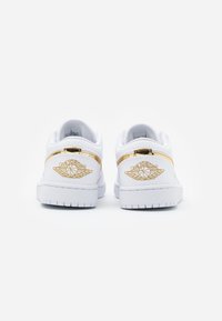 Baskets en cuir blanc avec un accent doré et le logo Air Jordan sur le talon. Texture lisse, design bas et semelle en caoutchouc.