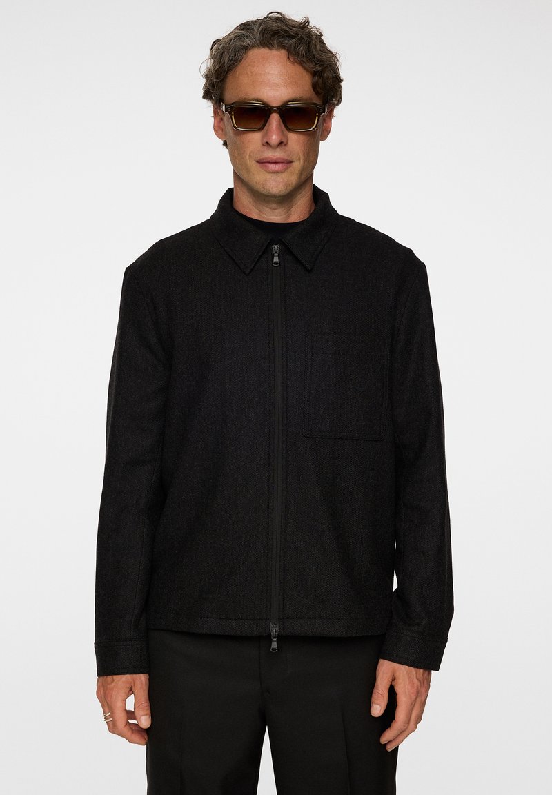 Svart jacka i ullblandning med dragkedja framtill, spetsig krage och en bröstficka, med en texturerad yta och rak passform.