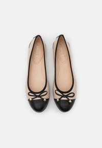 Des ballerines avec une tige nude et un bout en cuir noir. Elles présentent un accent en forme de nœud avec des perles dorées et une doublure intérieure lisse.