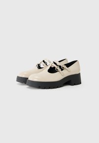 Zapatos Mary Jane de charol beige con suela negra texturizada, con puntera redondeada y dos correas ajustables con herrajes plateados.