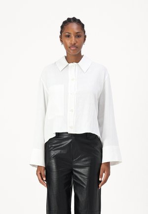 White cropped button-up shirt with a textured fabric, large collar, and single chest pocket. Paired with black leather wide-leg trousers.