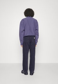 Lila sweatshirt med lång ärm och ribbade mudd, tillsammans med mörka denimjeans. Avslappnad passform, utan synliga mönster eller logotyper.