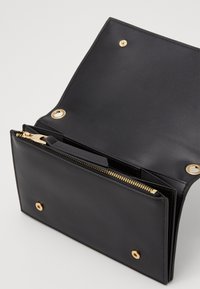 Portafoglio in pelle nera con scomparto con zip, accessori in hardware dorato e chiusura a scatto. Texture liscia con un design funzionale.