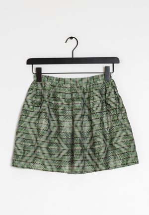 Jupe à motifs verts et noirs avec une taille élastique suspendue à un cintre noir sur fond blanc.