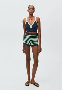 Námornícky pletený crop top s zelenými akcentmi, spárovaný s námorníckymi a zelenými pruhovanými šortkami. Modelka má na sebe čierne ploché sandále.
