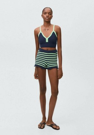 Top corto lavorato a maglia blu navy con accenti verdi, abbinato a pantaloni corti a righe blu e verdi. Il modello indossa sandali flat neri.
