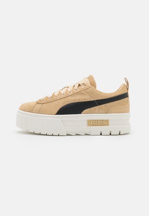 Beżowy zamszowy sneaker Puma z czarnym paskiem, grubą białą podeszwą, sznurowaniem z przodu i logo Puma po boku i na podeszwie.