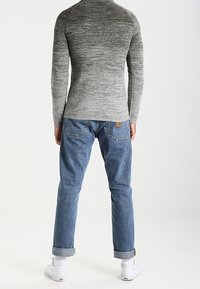 Grauer Strickpullover mit strukturiertem Design, kombiniert mit hellblauen Jeans. Sichtbar umgekrempelte Ärmelbündchen und weiße Sneaker. Sauberer, lässiger Look.