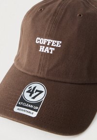 Καφέ υφασμάτινο καπέλο με κεντημένο το λευκό κείμενο «COFFEE HAT», με καμπυλωτό γείσο και ετικέτα που προσαρμόζει το μέγεθος με την ένδειξη «'47 CLEAN UP».