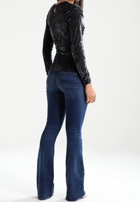 Svart sammet långärmad topp med blommönster och nyckelhålsgång, i kombination med blå utsvängda jeans med bakfickor och lätt blekning.