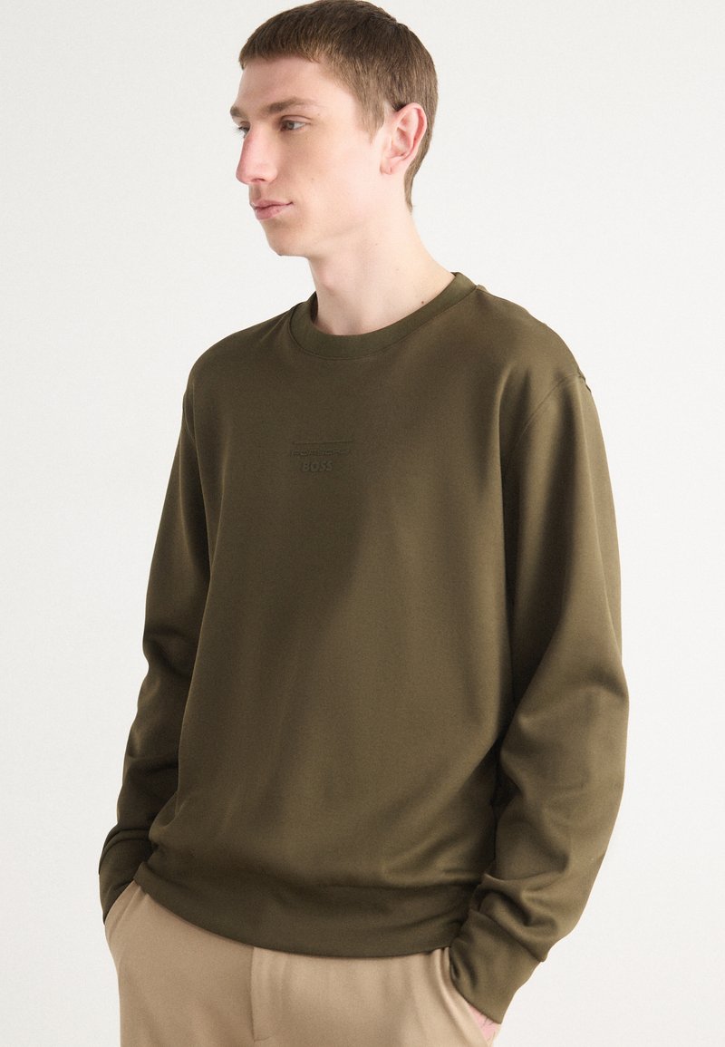 Sweat-shirt vert olive à manches longues, col rond, avec un discret logo en relief sur la poitrine, fabriqué à partir d'un tissu doux et lisse.