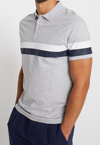 Polo gris en mélange de coton, doté de manches courtes, d'une patte de boutonnage à trois boutons et de rayures horizontales bleu marine et blanches sur la poitrine.