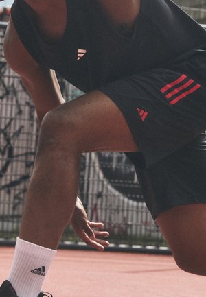 Athlet in schwarzen Adidas-Shorts und Shirt mit pinken Streifen, weißen Adidas-Socken, hockt auf der Außenbahn mit ausgestreckter Hand.