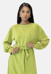 Robe vert citron à manches longues en tissu lisse, avec un col rond et une ceinture nouée à la taille.
