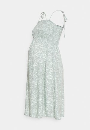 Lysegrøn graviditetstunika med hvidt bladtryk, tynde skulderstropper og smockdetaljer på overdelen, der falder ned i et knælængde skørt.