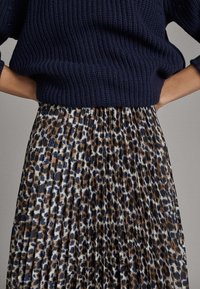 Marineblauw gebreid topje met ribbelstructuur, gecombineerd met een plissérok met een bruin- en blauwe luipaardprint.