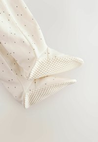 White baby socks with small black dots, featuring textured rubber grips on the soles for anti-slip safety.