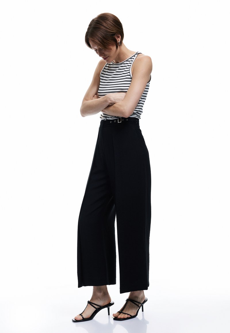 Un pantalon large noir associé à un débardeur rayé noir et blanc. Un tissu transparent, une taille haute et des talons noirs à lanières complètent l'ensemble.