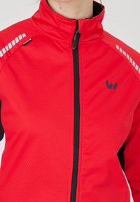 Giacca sportiva rossa con colletto alto, zip nera e dettagli riflettenti. Presenta un tessuto testurizzato e un logo sul petto.