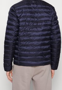 Giacca puffer blu marina con design a greche orizzontali, tessuto lucido leggero, colletto alto e logo GANT sul retro.