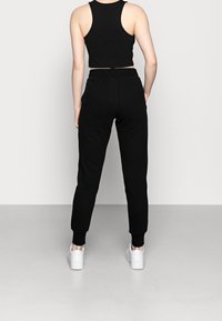 Svart kortärmad topp och matchande sweatpants, tillverkade av mjukt tyg. Byxorna har elastiska muddar och sidofickor. Vita sportskor.