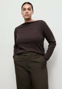 Maglione lungo a maniche lunghe di un marrone scuro con un colletto a barca alto, abbinato a pantaloni verde oliva a vita alta, caratterizzati da una texture liscia.