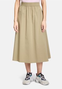 Khaki, middellange rok met een elastische tailleband, gemaakt van lichtgewicht stof. Gecombineerd met multikleurige sneakers met veters.
