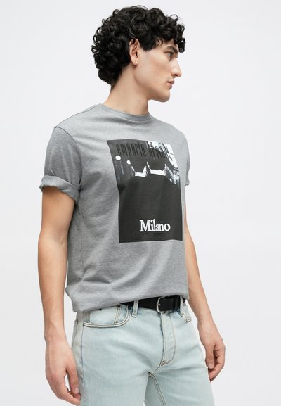 Γκρι βαμβακερό t-shirt με ρεβέρ στα μανίκια, διαθέτει ασπρόμαυρο γραφικό σχέδιο και τη λέξη "Milano" από κάτω, συνδυασμένο με ανοιχτόχρωμα τζιν.