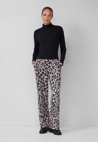 Črni rebrasti pulover s turtleneck ovratnikom, v kombinaciji z širokimi hlačami z leopardjim vzorcem. Hlače imajo žepe in kontrastni črn pas.
