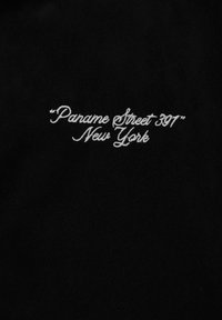 Black fabric featuring white embroidered text: “Parame Street 397” New York, in a cursive font, centered on the material.