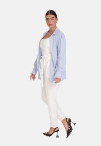 Camicia azzurro chiaro con texture a coste, top bianco aderente, pantaloni bianchi su misura e décolleté nere con tacco metallico curvo.